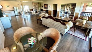 A spacious living area with a sofa, two wicker chairs, a glass coffee table with a floral centerpiece, a stone accent wall, and a bookshelf filled with books. - Shangrila  Oceanfront Retreat | 4 Ensuite Suites & 360° Views (Pender Island)