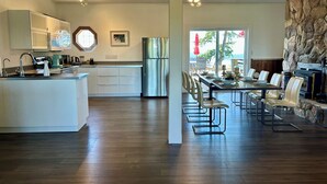 A modern kitchen with a central island, stainless steel appliances, and a dining area with a stone accent wall and outdoor view. - Shangrila  Oceanfront Retreat | 4 Ensuite Suites & 360° Views (Pender Island)