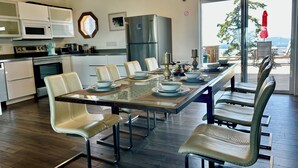 A modern kitchen with white cabinets, stainless steel appliances, and a dining area with a glass table and leather chairs. - Shangrila  Oceanfront Retreat | 4 Ensuite Suites & 360° Views (Pender Island)