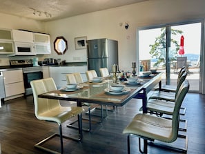 Una cocina moderna con armarios blancos, electrodomésticos de acero inoxidable y un comedor con mesa de vidrio y sillas de cuero.