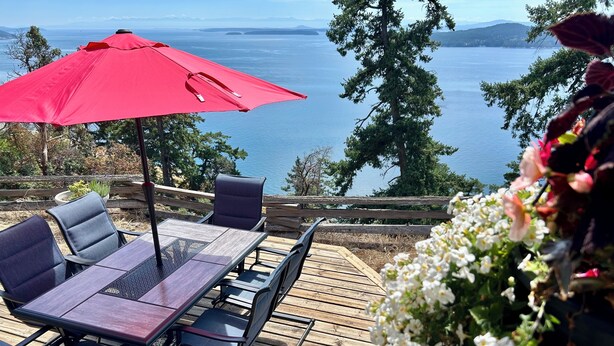 A deck with a table and chairs, a red umbrella, and a view of the sea. - Shangrila  Oceanfront Retreat | 4 Ensuite Suites & 360° Views (Pender Island)
