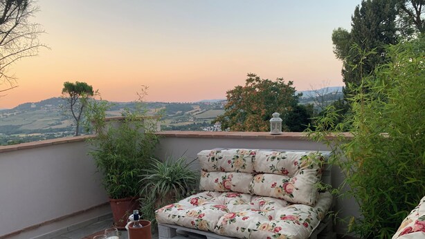 A balcony with a sofa and table, potted plants, and a view of the countryside.