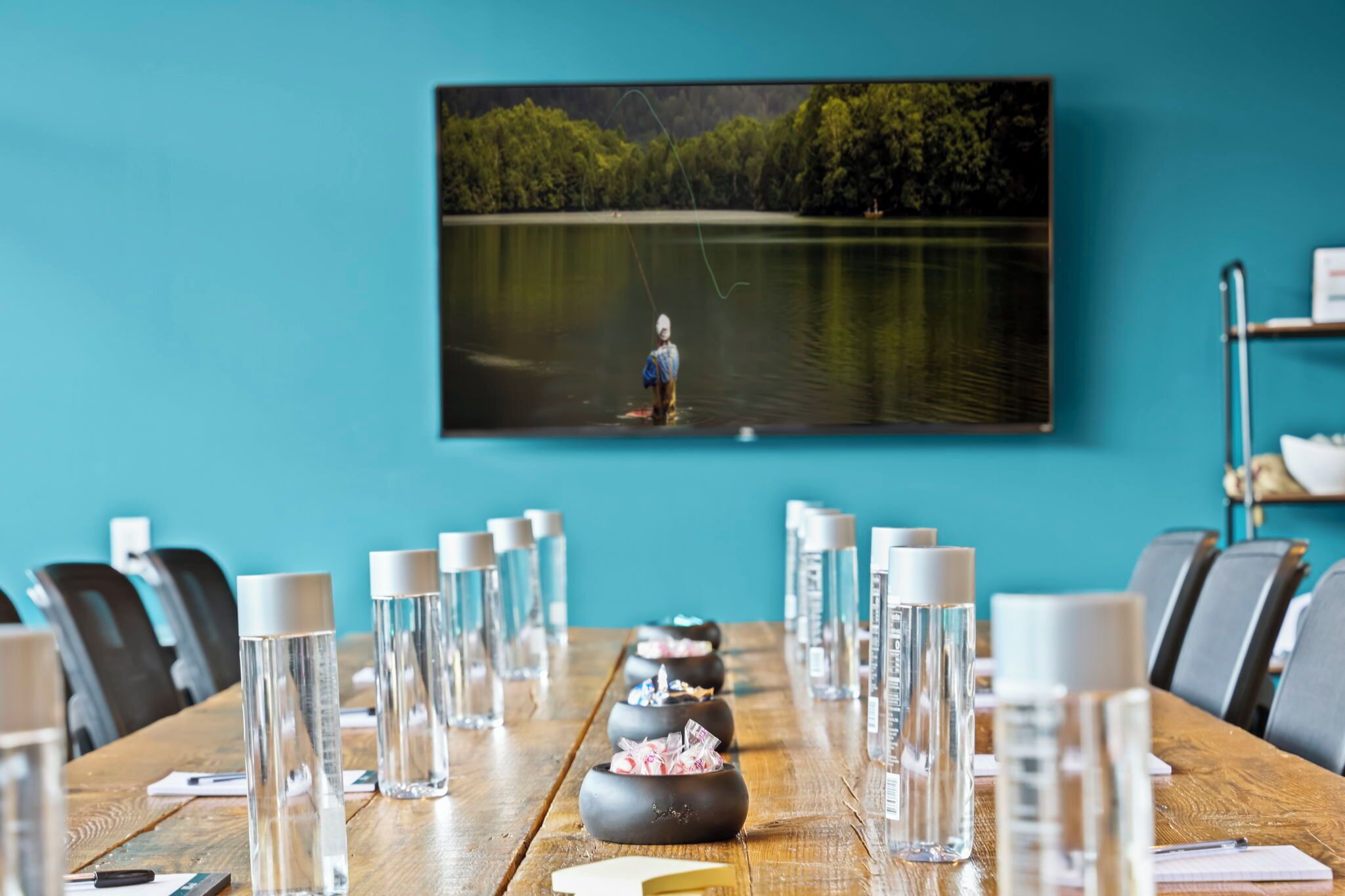 A conference room with a wooden table, water bottles, and a framed picture of a lake with a person fishing.