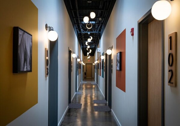 A hallway with a modern design, featuring a central light fixture, numbered doors, and a framed artwork on the left wall.
