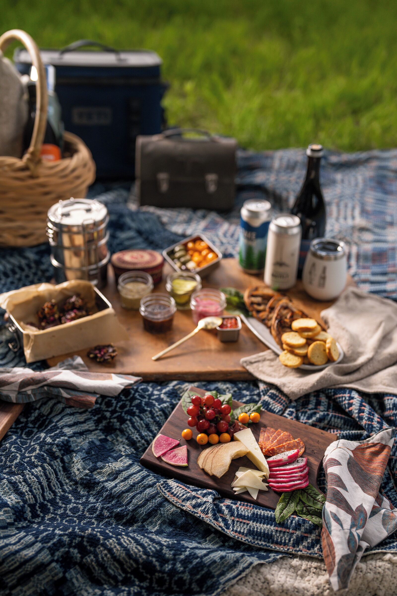 A picnic setup with food, drinks, and a blanket on grass.