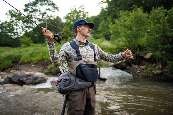 A person fishing by a river with a backpack and a fanny pack. - The Speckled Trout Outpost (Damascus)