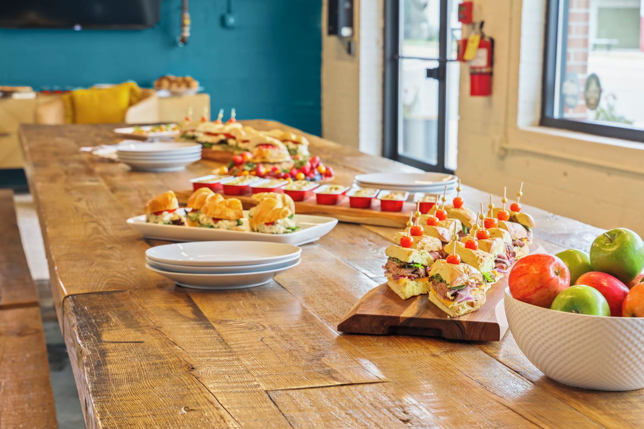 Une longue table en bois, sur laquelle sont disposés divers aliments, ainsi qu’un saladier rempli de fruits.