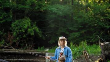 A person standing in a forested area with a river, holding a fishing rod.