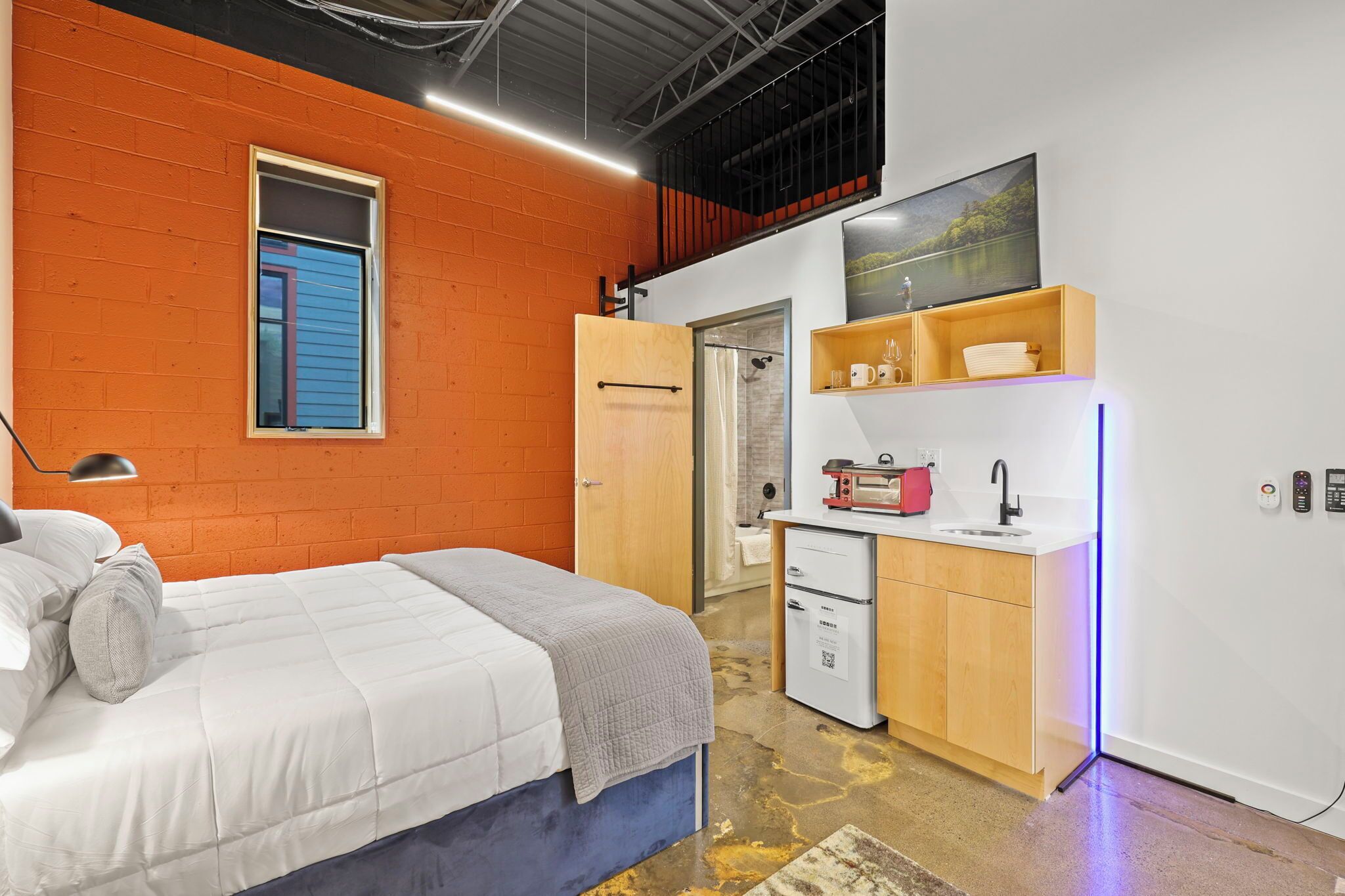 Un dormitorio pequeño con cama, una kitchenette y una ventana con persianas.