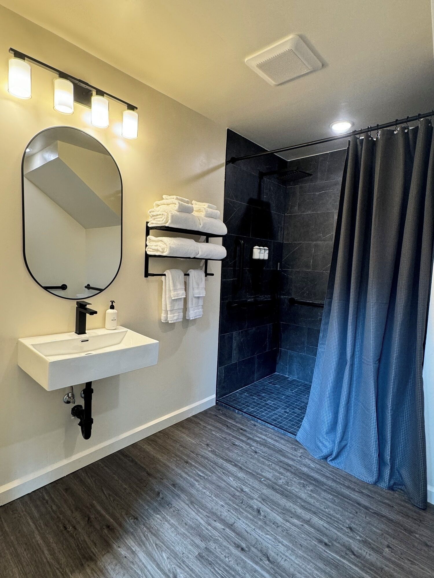 A modern bathroom with a vanity, a large mirror, a shower with a dark floor, and a curtain.