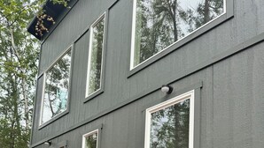 Een modern grijs gebouw met een houten terras, twee stoelen en potplanten.