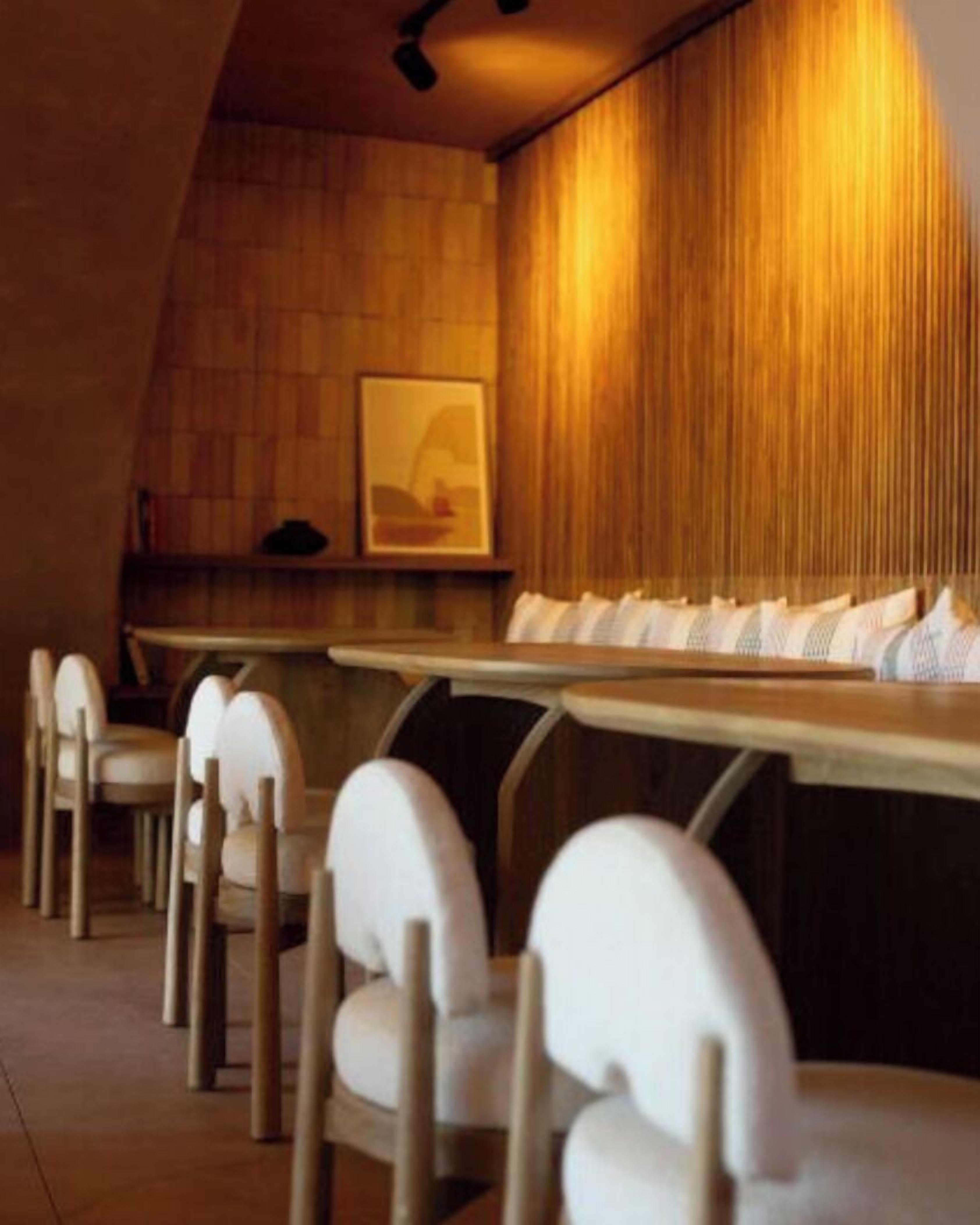 Een modern restaurant met een lange eettafel en witte stoelen.