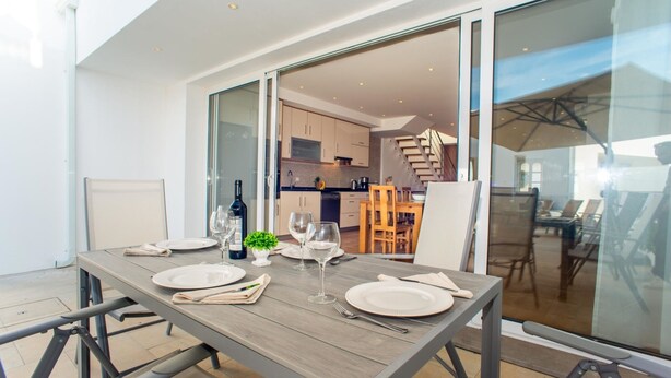 Een eethoek met een tafel voor vier personen, een keuken op de achtergrond en een schuifdeur naar een balkon.