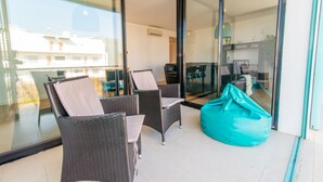 Ein Balkon mit Korbstühlen und einem Sitzsack, Glastüren zu einem Innenbereich mit Schreibtisch und Stuhl.