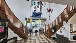 A hotel lobby with a checkered floor, wooden staircases, a chandelier, and a large window with a view. - KingBed+Kitchen+JacuzziTub+Pool+HotTub+Sauna (Oro)