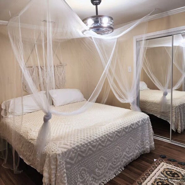 A bedroom with a four-poster bed, a canopy, a ceiling fan, a large mirror, and a patterned rug.