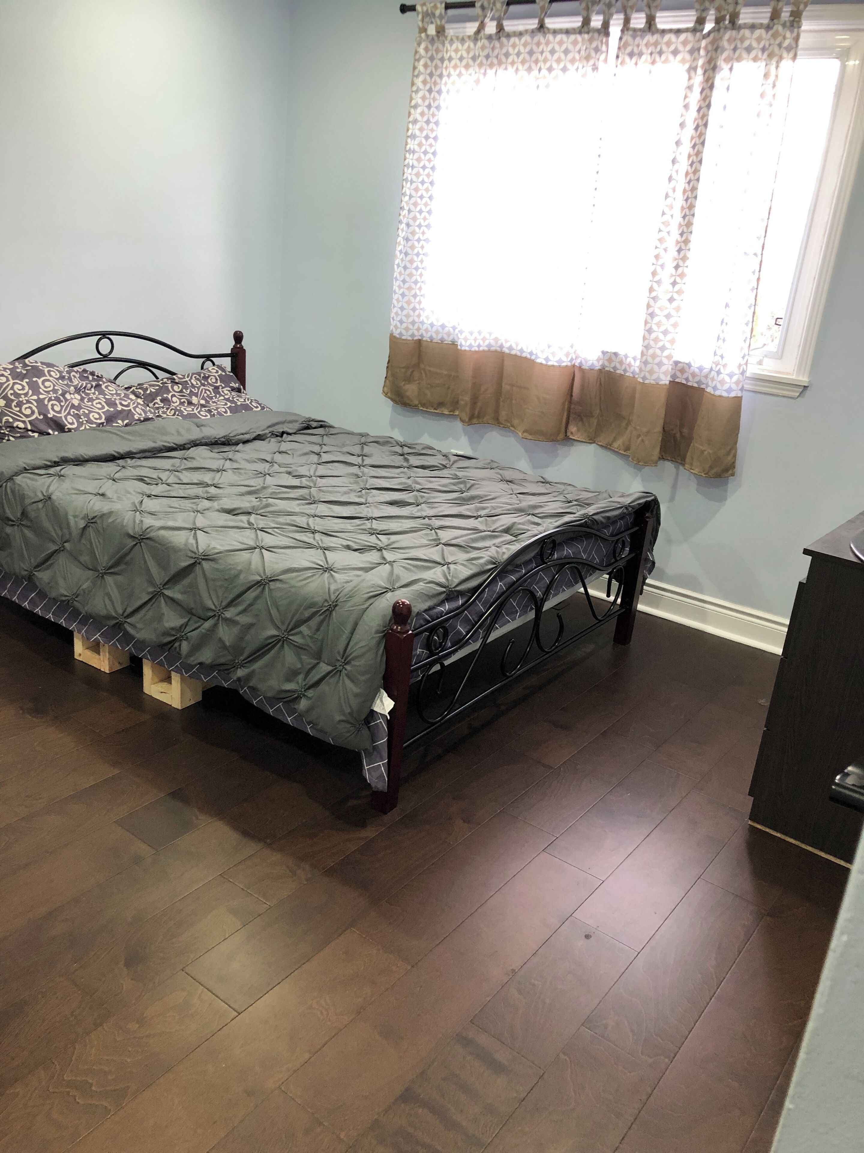 A bedroom with a bed, wooden headboard, and a window with patterned curtains.