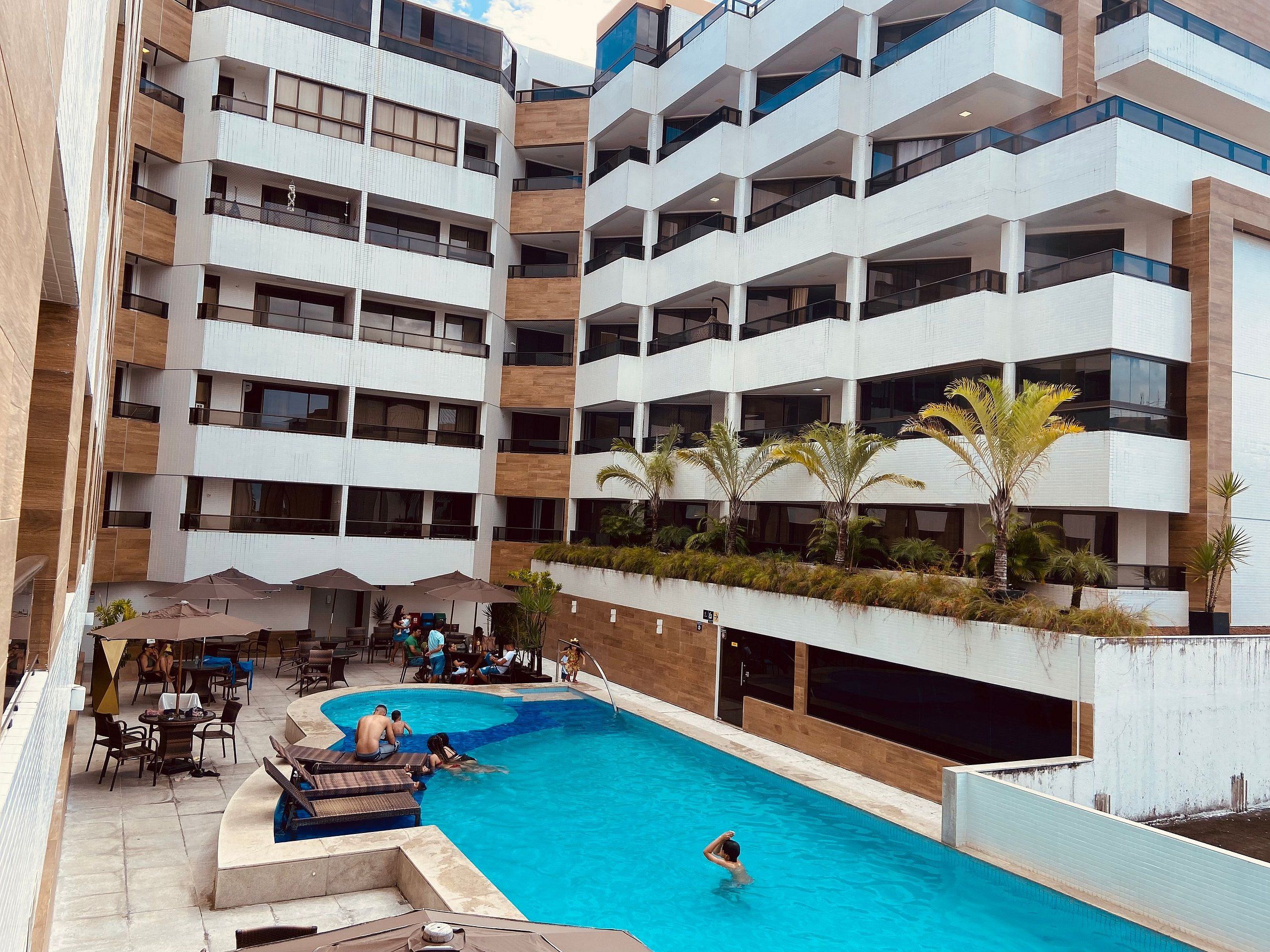 Un hotel moderno con piscina en la azotea, mobiliario exterior y varios balcones.