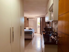 A modern kitchen with a stove, sink, and cabinets. There is a bed with a white mattress and a towel on it. The room has a sliding glass door leading to a balcony. - Gold Flat by Apartamentos Jampa (João Pessoa)