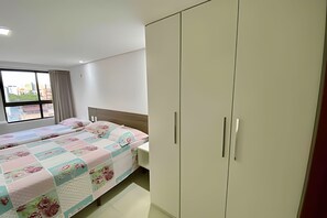Un dormitorio con dos camas, un armario y una ventana con vistas a edificios.