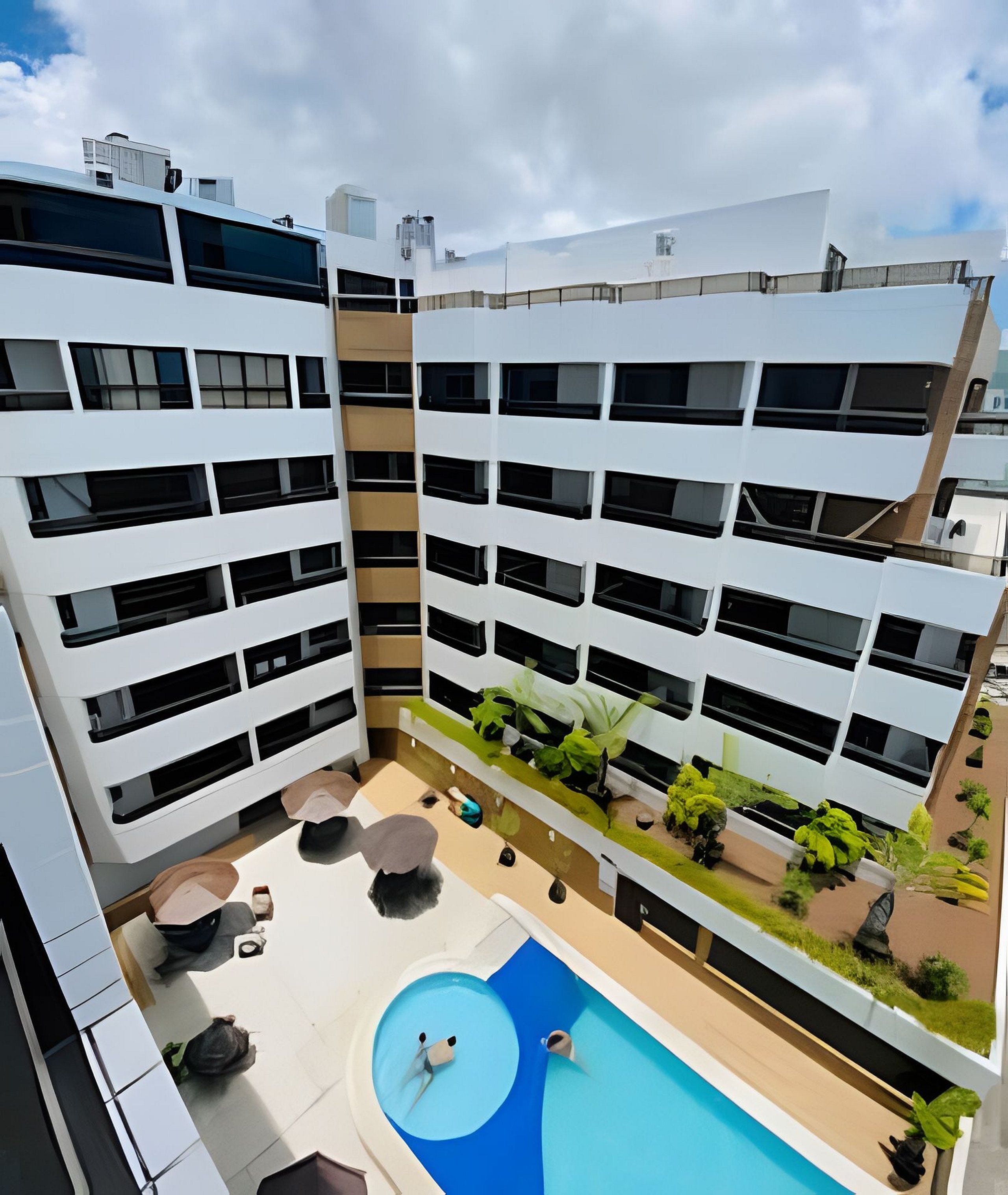A modern building with multiple balconies, a rooftop pool, and outdoor seating areas.