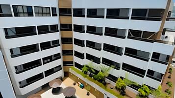 A modern building with multiple balconies, a rooftop pool, and outdoor seating areas.