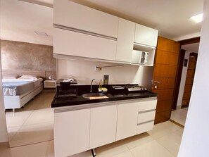 Una cocina compacta con armarios blancos, estufa y microondas.