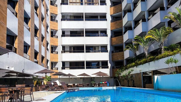 Un hotel moderno con piscina, mobiliario exterior y varios balcones.