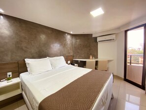 A hotel room with a large bed, a bedside table with a plant, a small desk with a chair, and a view of the outside through a balcony door. - Gold Flat by Apartamentos Jampa (João Pessoa)