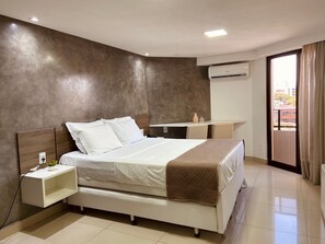 A modern hotel room with a bed, bedside table, and a desk with a chair. - Gold Flat by Apartamentos Jampa (João Pessoa)