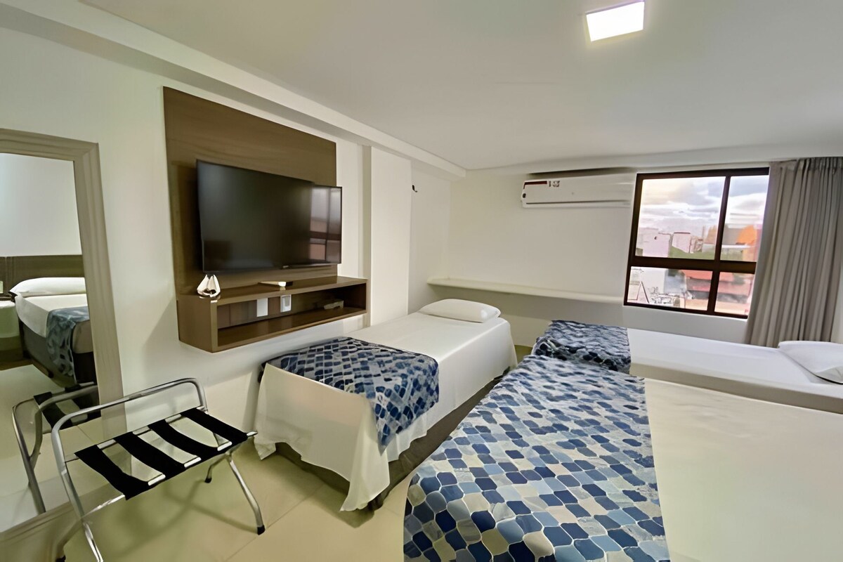 A hotel room with a bed, a TV, a chair, and a window with a city view.