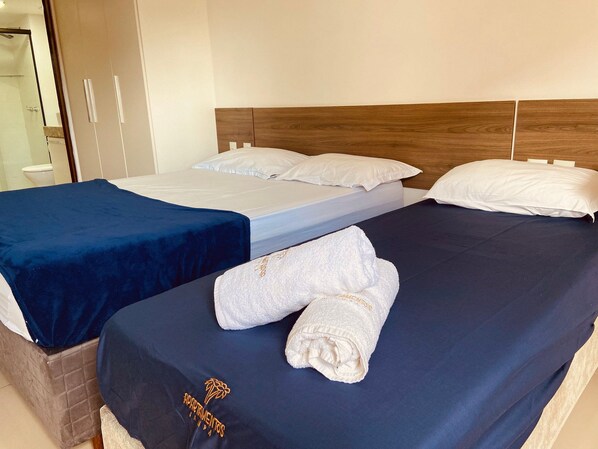 Une chambre d’hôtel avec deux lits, chacun recouvert d’une couverture bleue et agrémenté d’oreillers blancs. Une serviette avec un logo est posée sur l’un des lits.