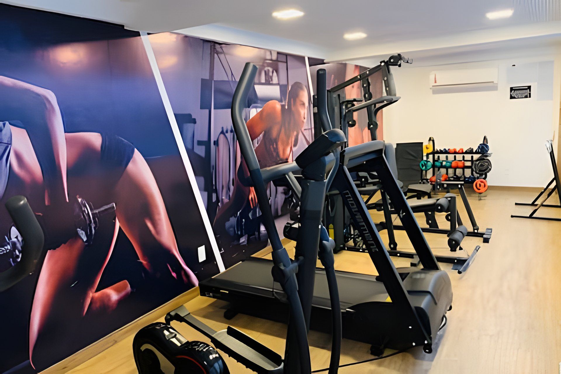 Academia com equipamentos de ginástica, esteira e parede com pôster.