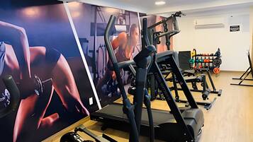 Academia com equipamentos de ginástica, esteira e parede com pôster.