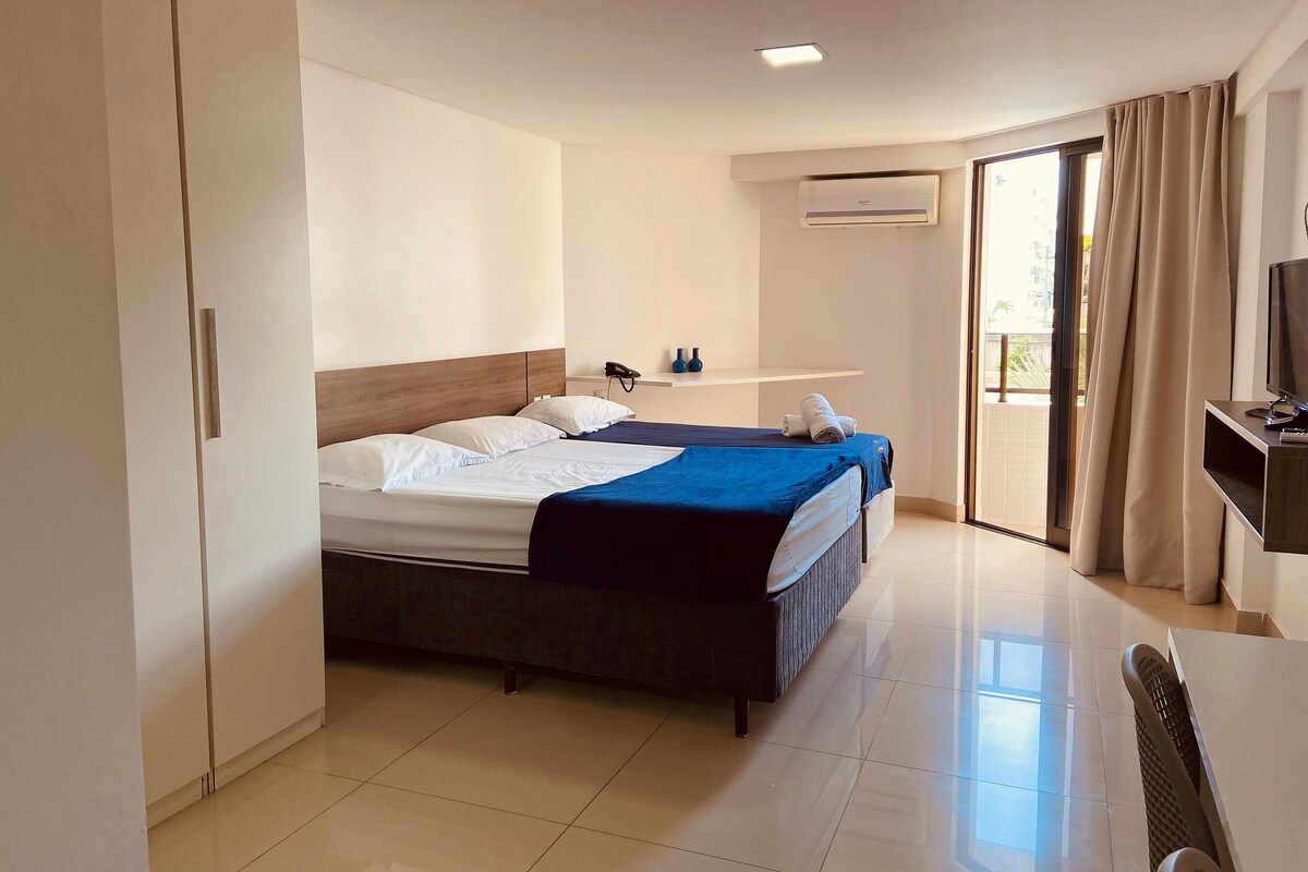 A hotel room with a bed, a desk, a chair, a TV, and a bathroom.