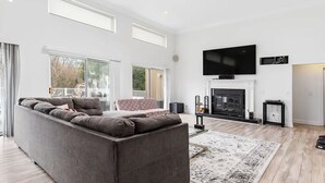 A modern living room with a large grey sofa, a fireplace, and a flat-screen TV mounted above it. - Hamptons getaway (East Quogue)