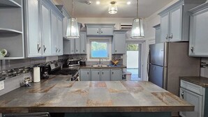 Een moderne keuken met grijze kastjes, een centraal eiland, roestvrijstalen apparatuur en hangende lampen.