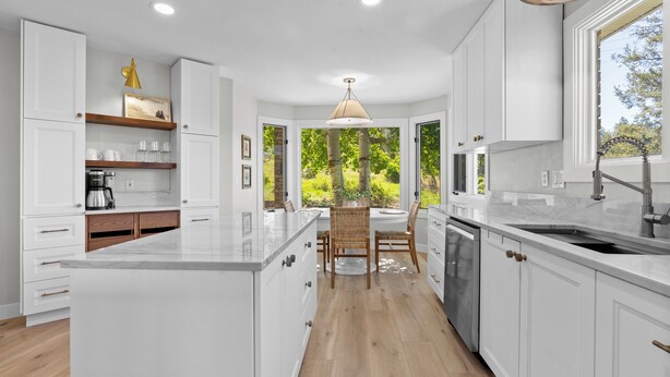 A modern kitchen with white cabinetry, a central island, and a view of greenery outside.