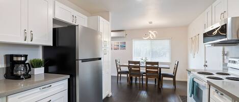 A modern kitchen with white cabinets, stainless steel appliances, and a dining area with wooden chairs.