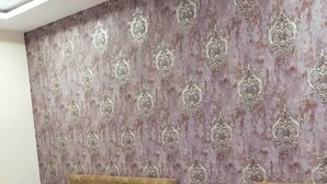 A hotel room with two single beds, a patterned wallpaper, a ceiling fan, and a marble floor. - Hotel Somnath Inn (Ujjain)