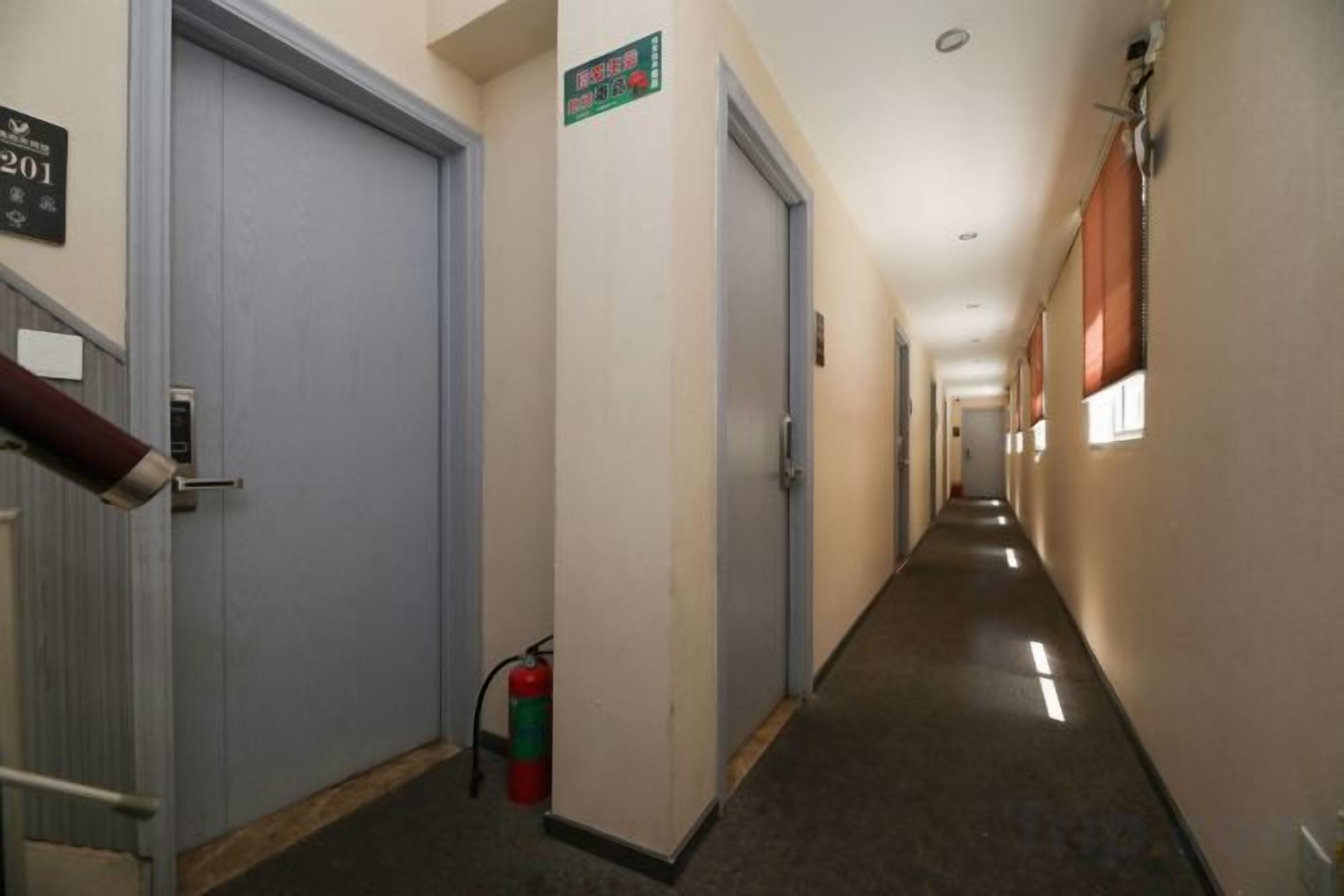A hallway with doors, a fire extinguisher, and a sign indicating a room number.
