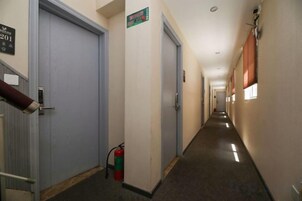 Un pasillo con puertas, un extintor y un cartel con número de habitación.
