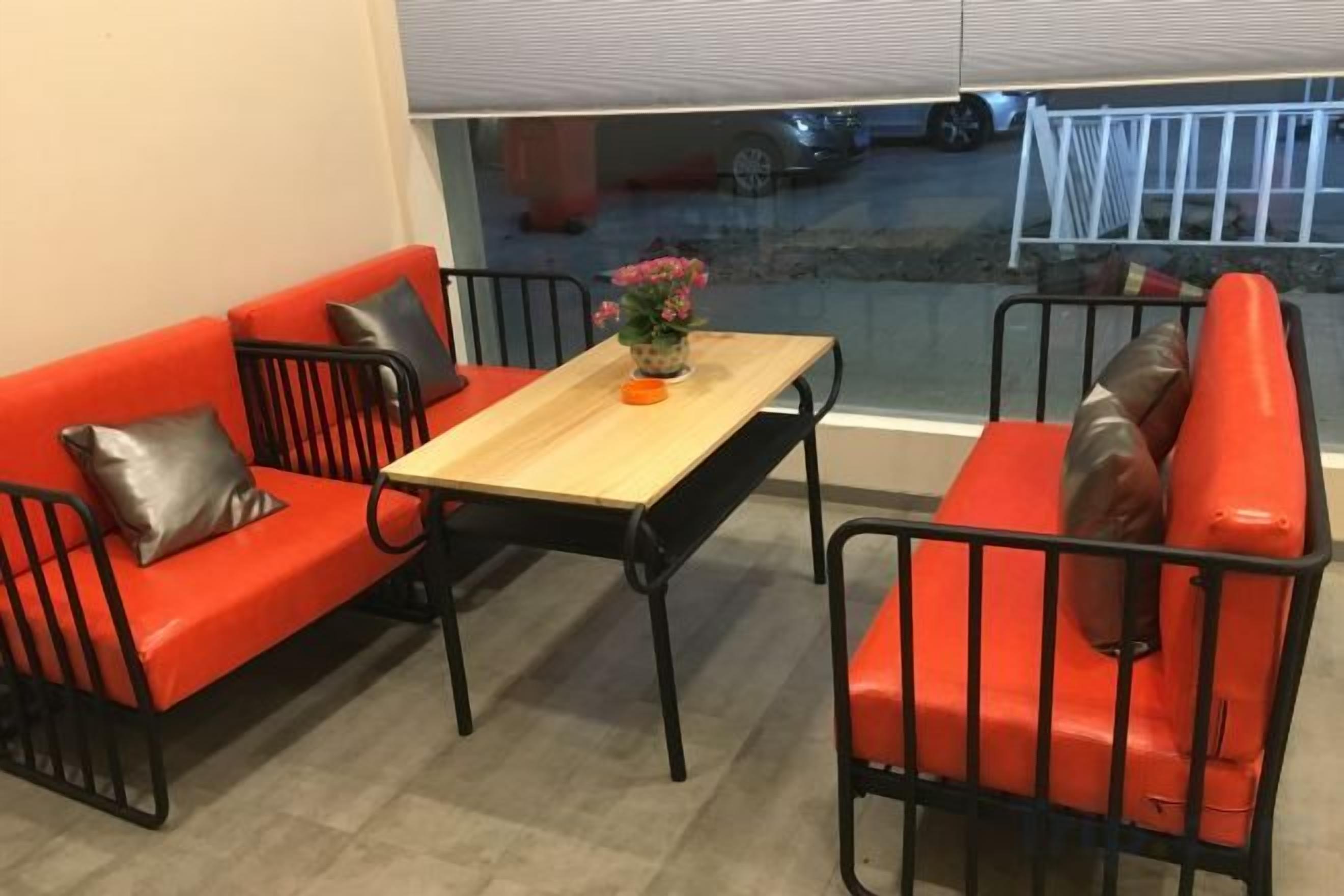 Une pièce avec un canapé rouge, une table en bois et une vue sur la rue par une fenêtre.