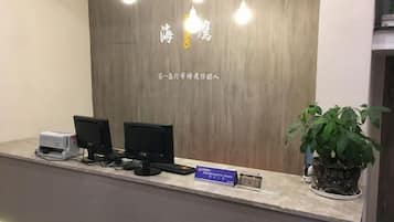A reception desk with a wooden backdrop, two monitors, a printer, and a potted plant.