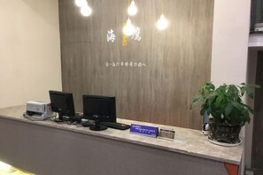 A reception desk with a wooden backdrop, two monitors, a printer, and a potted plant. - Haiying Hotel (Xiangshan)