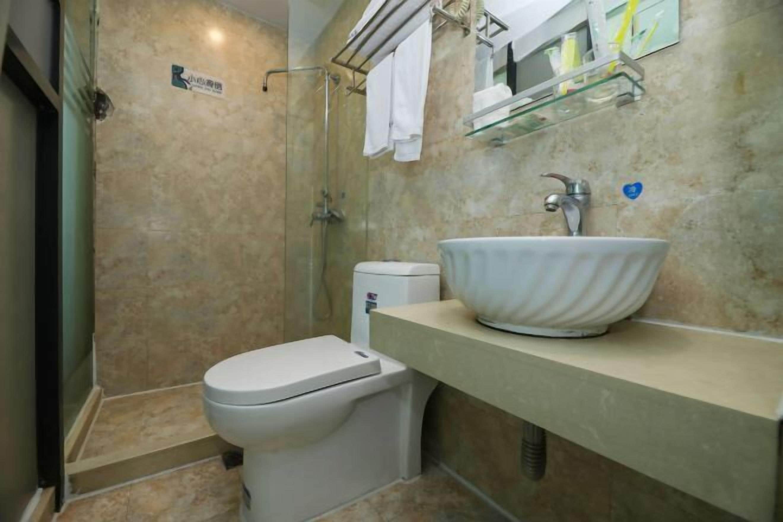 Um banheiro moderno com parede em azulejos bege, pia branca, box de vidro e vaso sanitário.