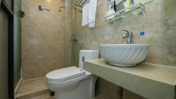 Um banheiro moderno com parede em azulejos bege, pia branca, box de vidro e vaso sanitário.
