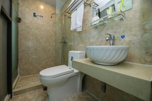 Un baño moderno con pared de azulejos color beige, un lavamanos blanco, una mampara de cristal para la ducha y un inodoro.