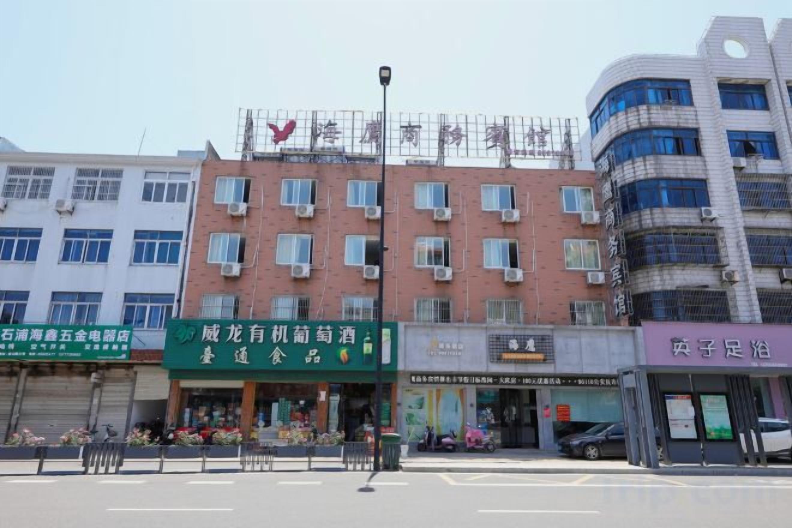A multi-story building with a row of shops on the ground floor, including a green sign for a restaurant and a purple sign for a store.