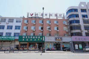 Un edificio de varios pisos con una hilera de comercios en la planta baja, incluyendo un letrero verde para un restaurante y uno morado para una tienda.